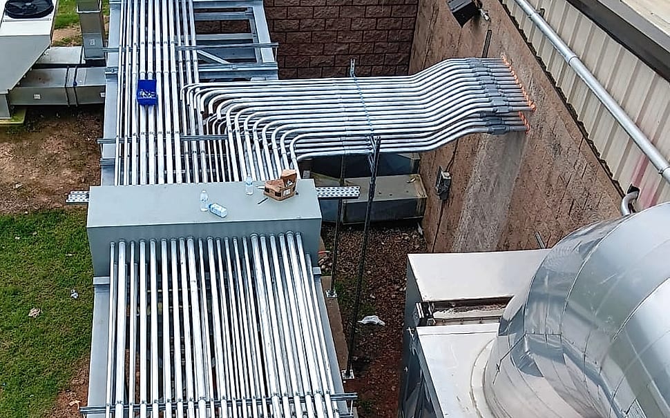 Long exterior conduit rack on strut supports carrying a parallel raceway bank, with a matched group of offset bends turning into the building wall