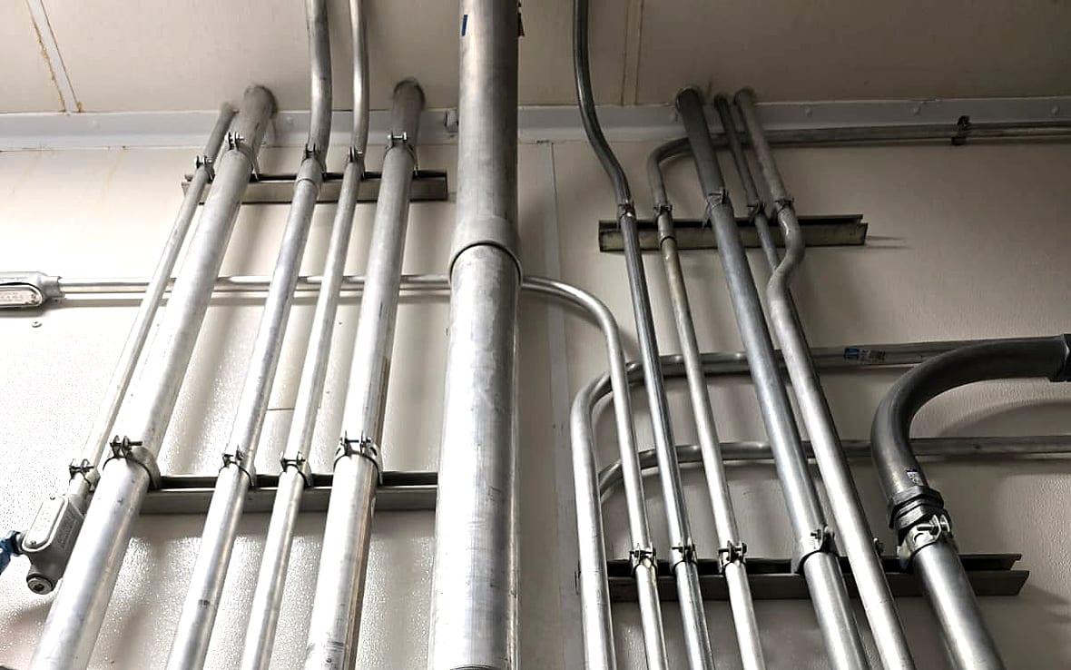 Rigid conduit feeding a 400 amp motor control center labeled for vat wash service, with strut supports, clamps and circuit identification tags