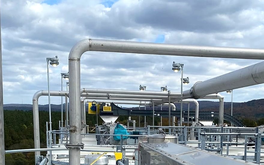 Elevated process platform with stainless steel piping runs, storage tanks, conveyor and galvanized access catwalks at an industrial processing plant