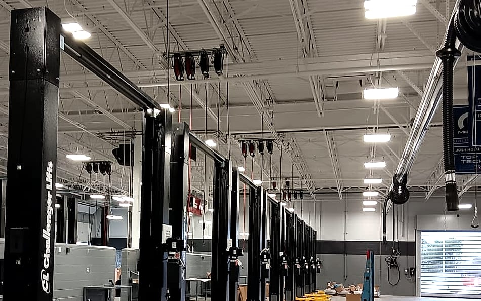Row of two-post vehicle lifts in a newly built service facility, with overhead power reels, exhaust extraction and high-bay lighting installed